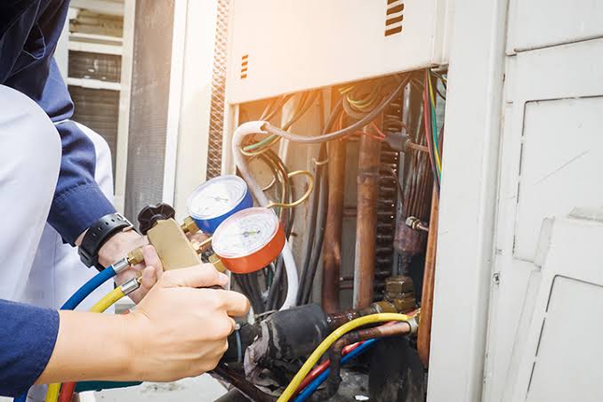 Technician using diagnostic gauges on outdoor HVAC equipment