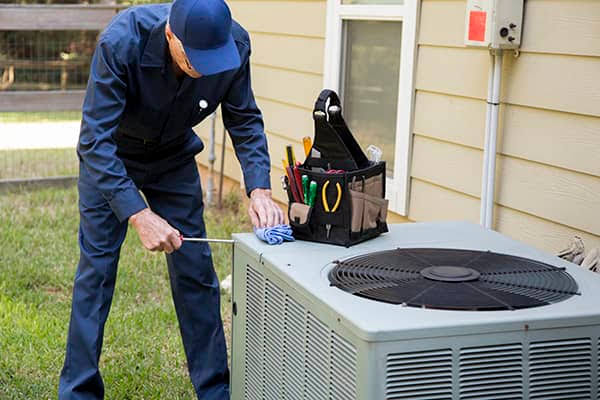 Technician performing routine maintenance on a residential outdoor HVAC condenser