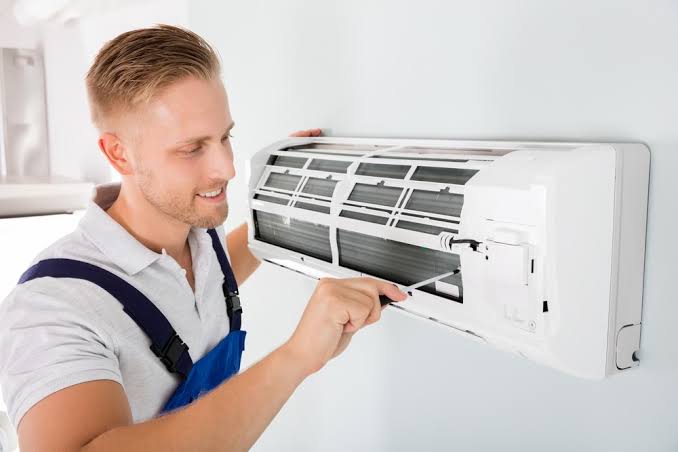 Technician checking a wall-mounted air conditioning control and filter